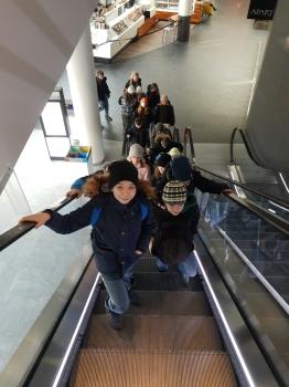 uczniowie wjeżdżają ruchomymi schodami w centrum handlowym