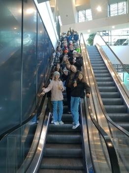 uczniowie zjeżdżają w dół ruchomymi schodami w centrum handlowym